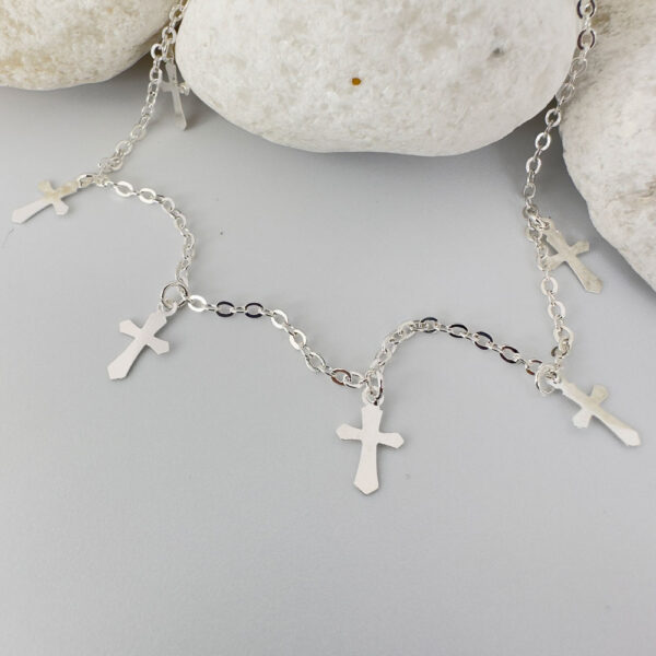 Silver anklet with three silver crosses equally spaced around the chain on a white rock.