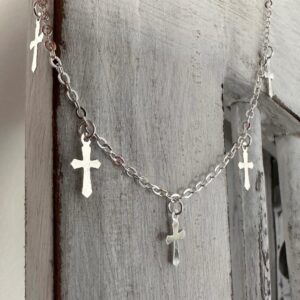 Gothic style silver anklet with five crosses around the chain, hanging off white washed wood.