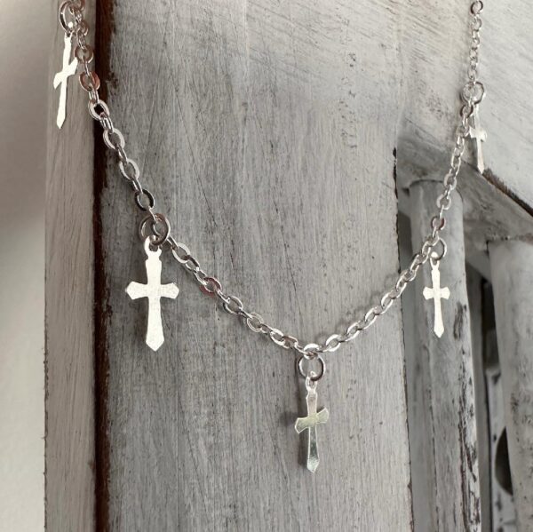 Gothic style silver anklet with five crosses around the chain, hanging off white washed wood.