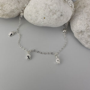 Stunning feminine silver anklet with tulip charms around the chain on a white rock.