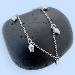 Stunning feminine silver anklet with tulip charms around the chain on a black rock.