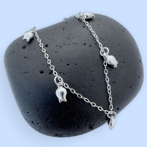 Stunning feminine silver anklet with tulip charms around the chain on a black rock.