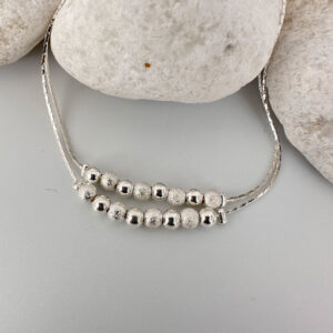 Silver anklet with a double chain with eight balls on a white rock.