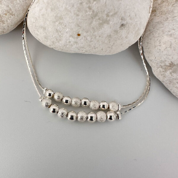 Silver anklet with a double chain with eight balls on a white rock.