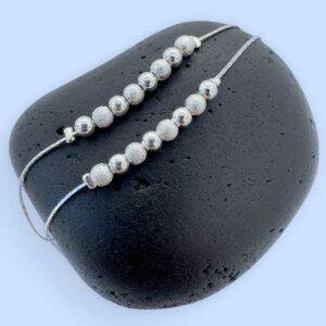 Double silver anklet chain both with eight silver balls on a black rock.