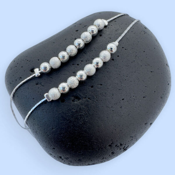 Double silver anklet chain both with eight silver balls on a black rock.