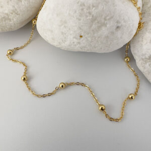 Gold chain with eight small gold balls on a white rock.