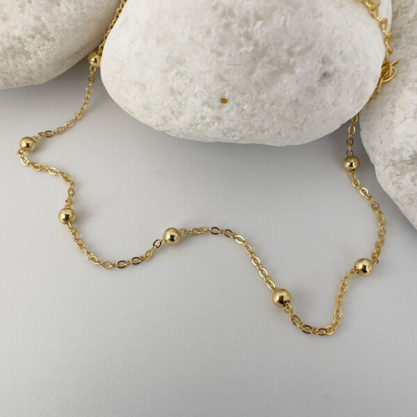 Gold chain with eight small gold balls on a white rock.