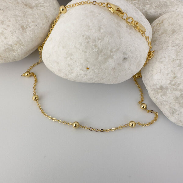 Gold chain with eight small gold balls on a white rock.