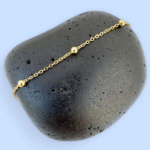 Gold chain with three small gold balls on a black rock.