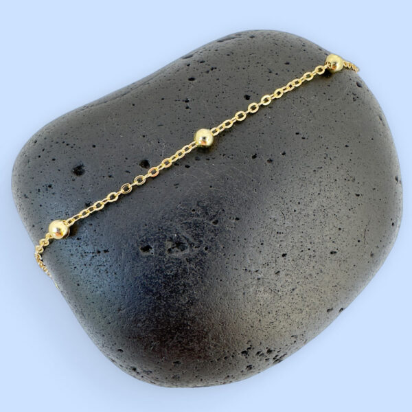 Gold chain with three small gold balls on a black rock.
