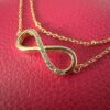 Close up of a gold infinity charm covered with cubic zirconia gems along one half, on a stunning gold ankle bracelet.