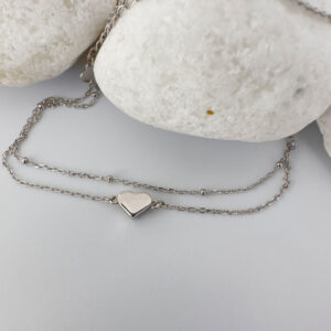 Dainty double ankle chain with a solid silver heart charm on a white rock.