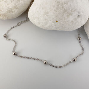 Dainty silver anklet with eight small balls spaced equally around the chain draped on white rocks.