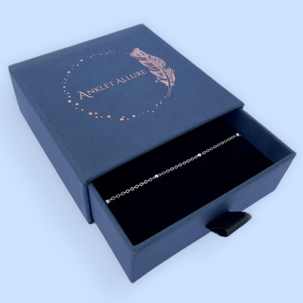 Silver anklet with equally spaced out small silver balls along the chain presented in a dark blue Anklet Allure gift box.