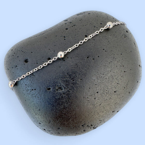 Silver anklet with equally spaced out small balls along the chain draped on three white rocks.