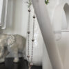 Sterling silver anklet with six evenly spaced balls around the chain hanging from the spout of a white watering can.