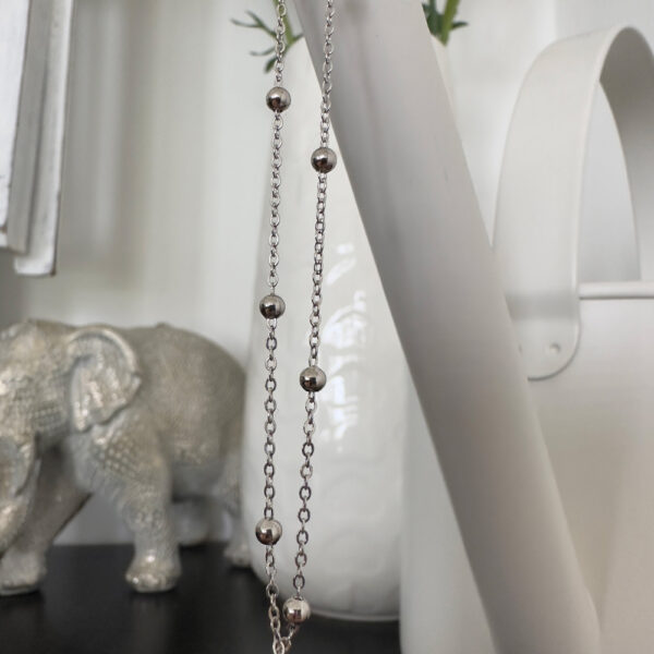 Sterling silver anklet with six evenly spaced balls around the chain hanging from the spout of a white watering can.