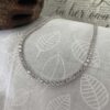 White diamond tennis anklet on grey and white leaf background.