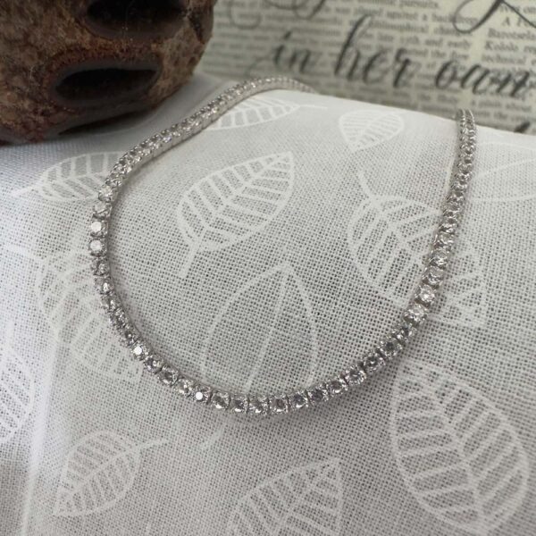 White diamond tennis anklet on grey and white leaf background.