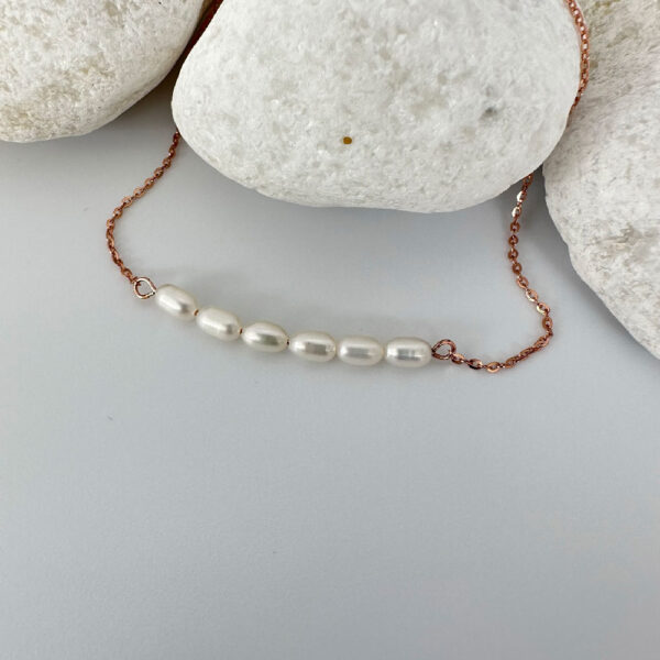 Stunning rose gold anklet with six freshwater pearls on a white rock.