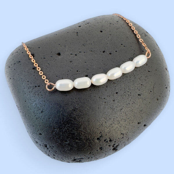 Rose gold anklet with six freshwater pearls sat on a black rock.