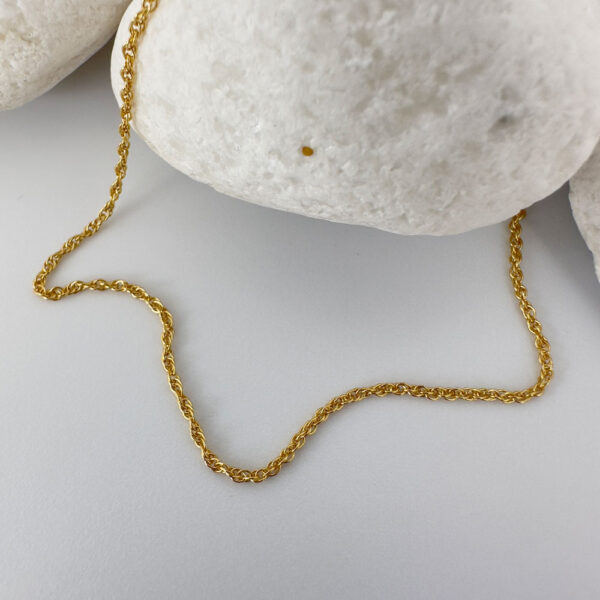 Simple gold anklet presented on a white rock.