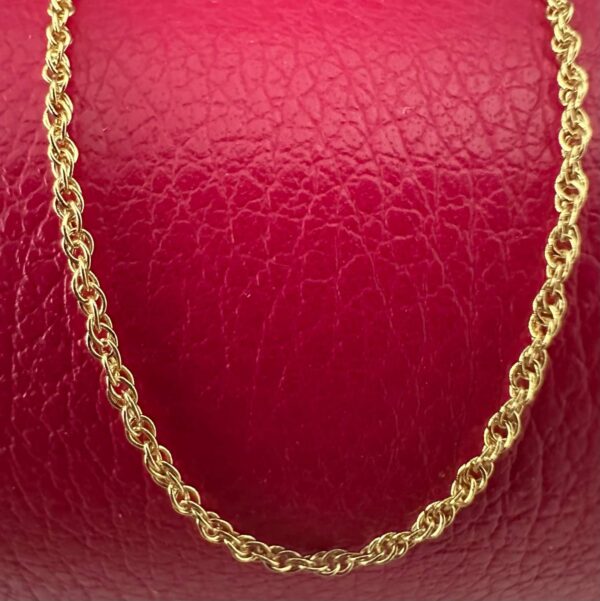 Close up of a simple gold anklet chain on a red background.