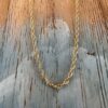 Looking up at a simple gold ankle bracelet hanging on a painted wood background with a beach chic feel.
