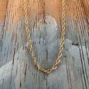 Looking up at a simple gold ankle bracelet hanging on a painted wood background with a beach chic feel.
