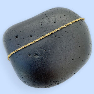 Dainty gold simple ankle bracelet presented on a black rock.