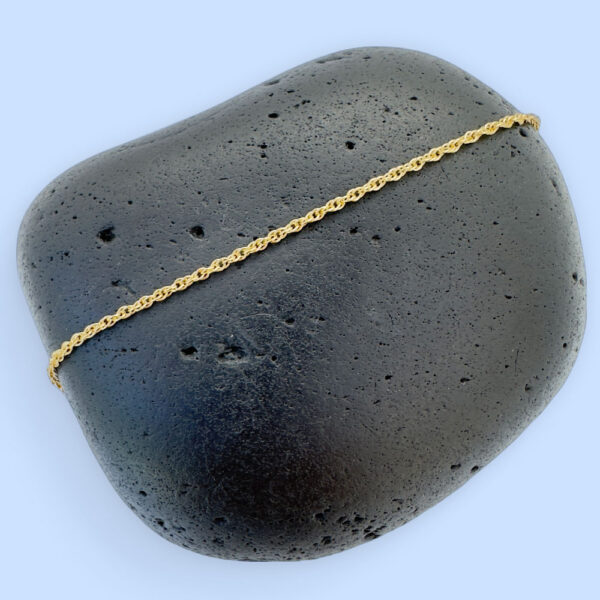 Dainty gold simple ankle bracelet presented on a black rock.