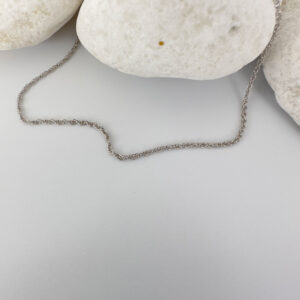 Plain silver anklet draped on three white rocks.