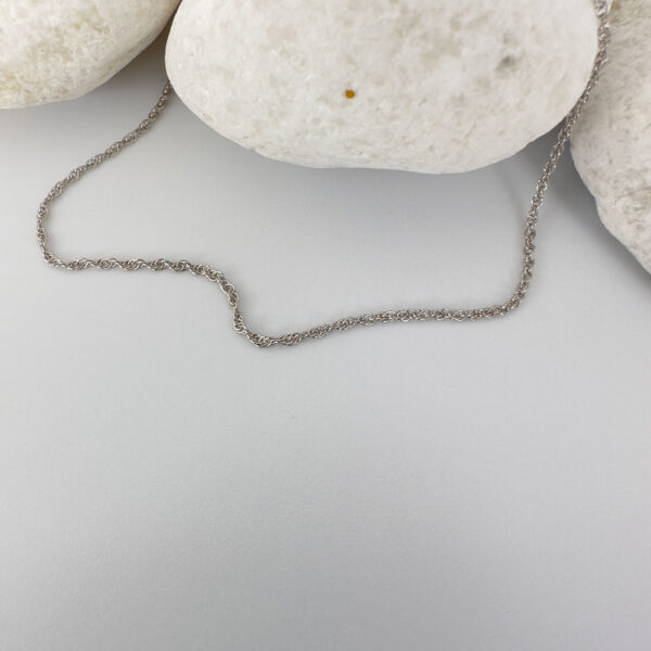 Plain silver anklet draped on three white rocks.