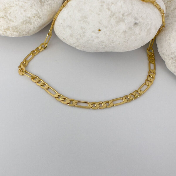 Elegant gold Figaro style ankle bracelet displayed on a white rock.