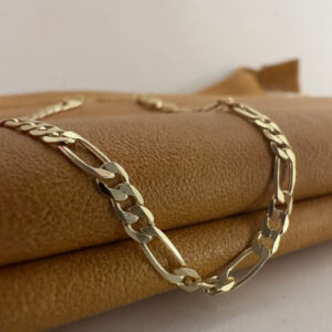 Stunning diamond cut figaro chain gold anklet pictured close up draped over a mustard coloured purse.