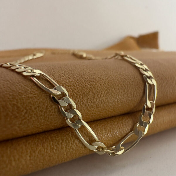 Stunning diamond cut figaro chain gold anklet pictured close up draped over a mustard coloured purse.