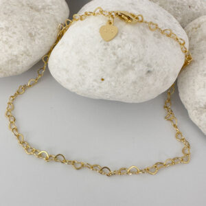Identical gold hearts interlinked to make a dainty anklet displayed on a white rock.