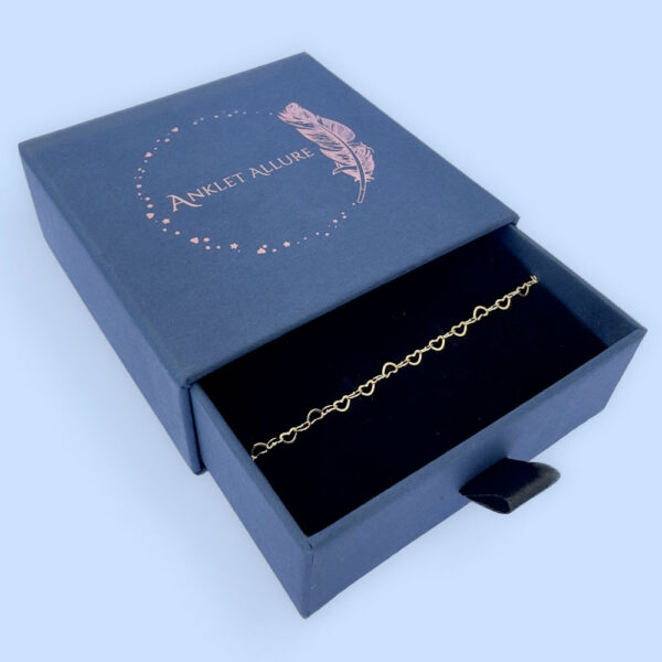 Identical gold hearts interlinked to make a dainty anklet presented in a dark blue Anklet Allure gift box.