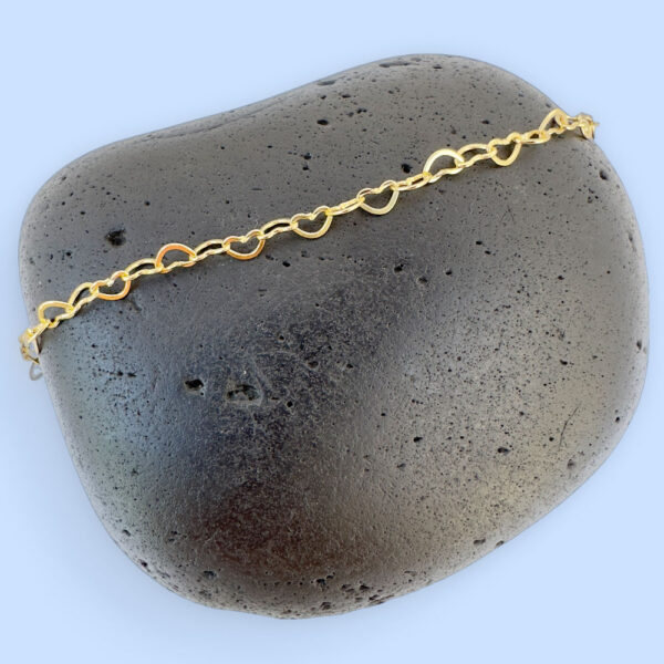 Identical gold hearts interlinked to make a dainty anklet displayed on a black rock.