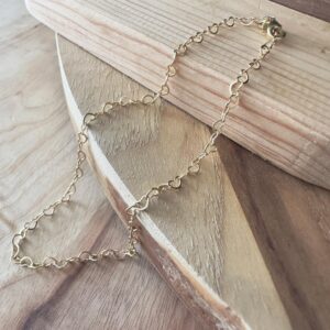Loving gold hearts interlinked to form a beautiful anklet, presented on wood.