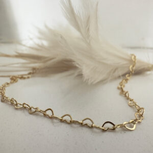Stunning gold anklet made of interlinking identical hearts draped over a white feather.
