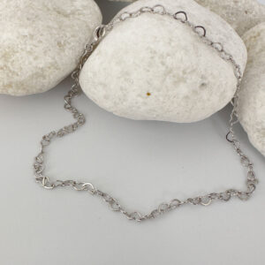 Identical silver hearts interlinked to make a dainty anklet displayed on a white rock.