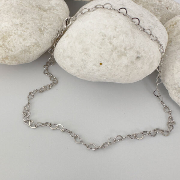 Identical silver hearts interlinked to make a dainty anklet displayed on a white rock.