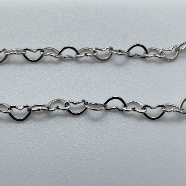 Close up of identical silver hearts interlinked to make a dainty anklet.