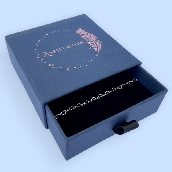 Identical silver hearts interlinked to make a dainty anklet presented in a dark blue Anklet Allure gift box.
