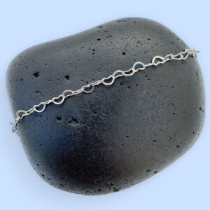 Identical silver hearts interlinked to make a dainty anklet displayed on a rock.