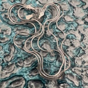 Triple chain sterling silver anklet curled up on a blue and silver background like spaghetti.