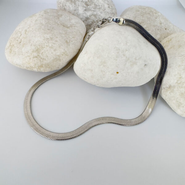 Thick silver snake chain anklet on white rocks.