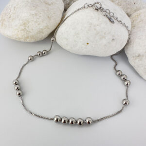 Silver anklet with identical balls floating around the chain, on white rocks.